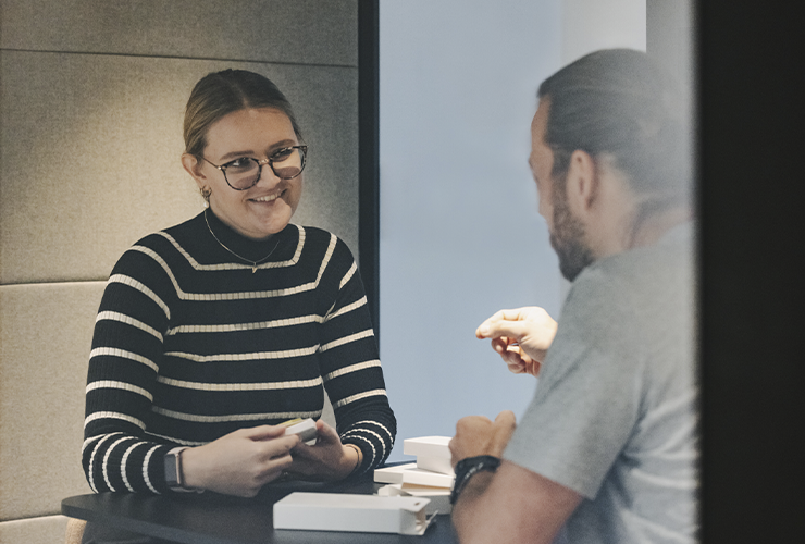 Two colleagues having a friendly conversation at a table with small white boxes.