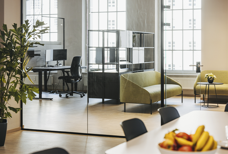 Bright office space with green seating, workstations, and a bowl of fruit on a table in the foreground.