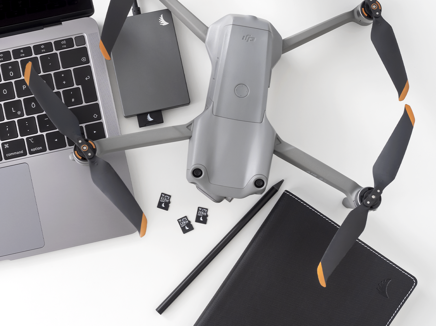 3 AV PRO microSD V30 memory cards placed on a table next to a notebook, a laptop and a drone