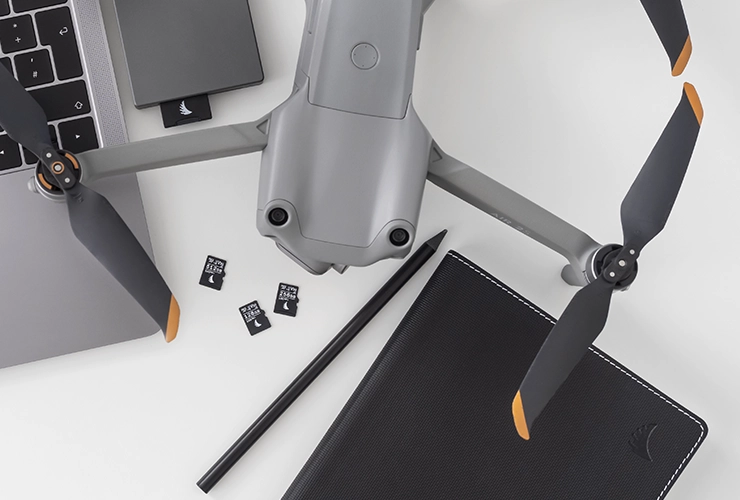 3 AV PRO microSD V30 memory cards placed on a table next to a notebook, a laptop and a drone